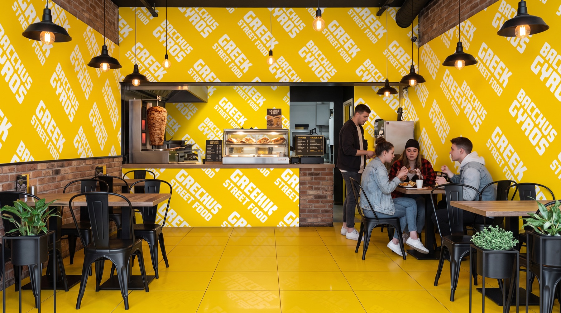 Salle du restaurant : mur typographique jaune, sol jaune et cuisine ouverte